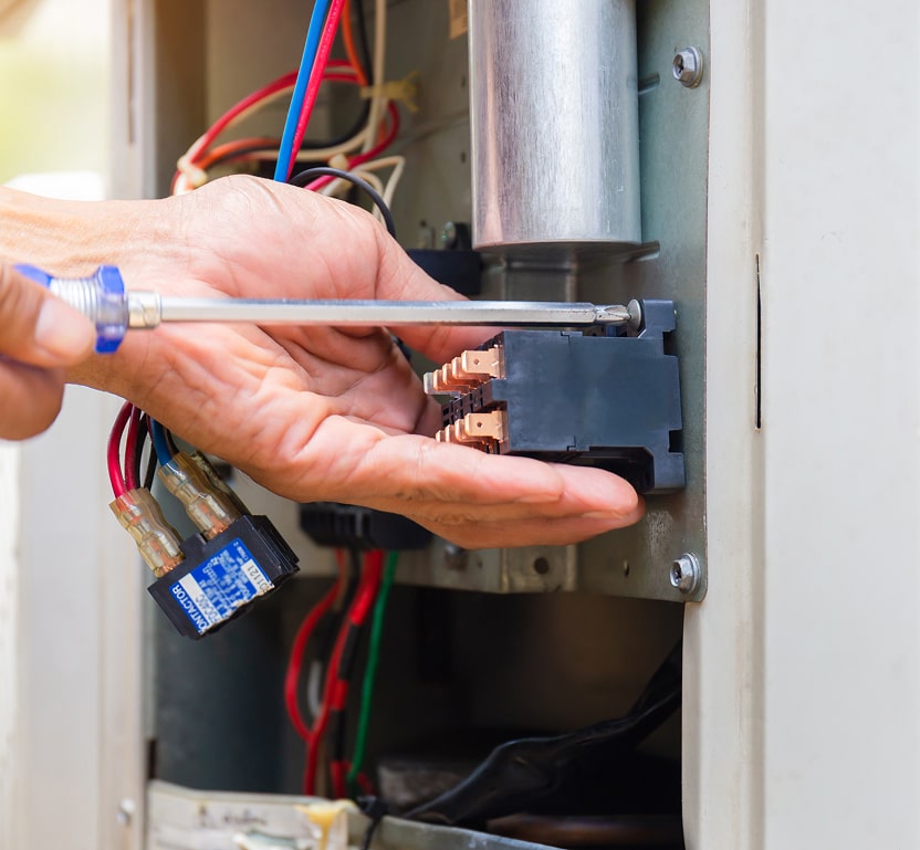 A worker using a screwdriver on a furnace electrical area.