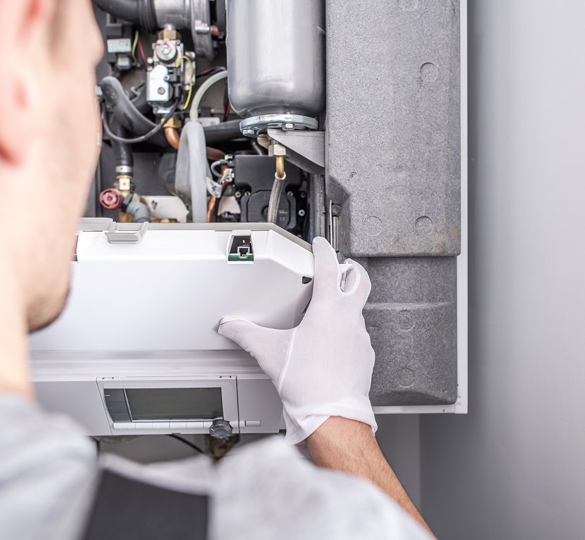 A worker working on a furnace unit. All the inner workings and parts are seen beneath the cover