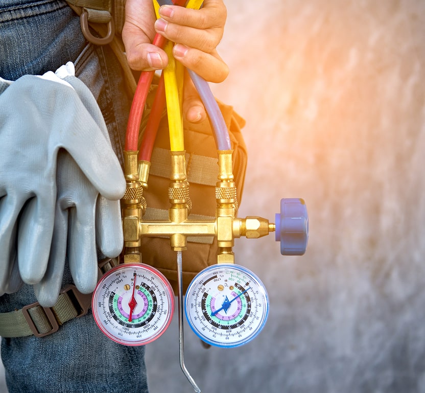 A closeup of a workers AC gauges on his toolbelt next to some gloves and a pack